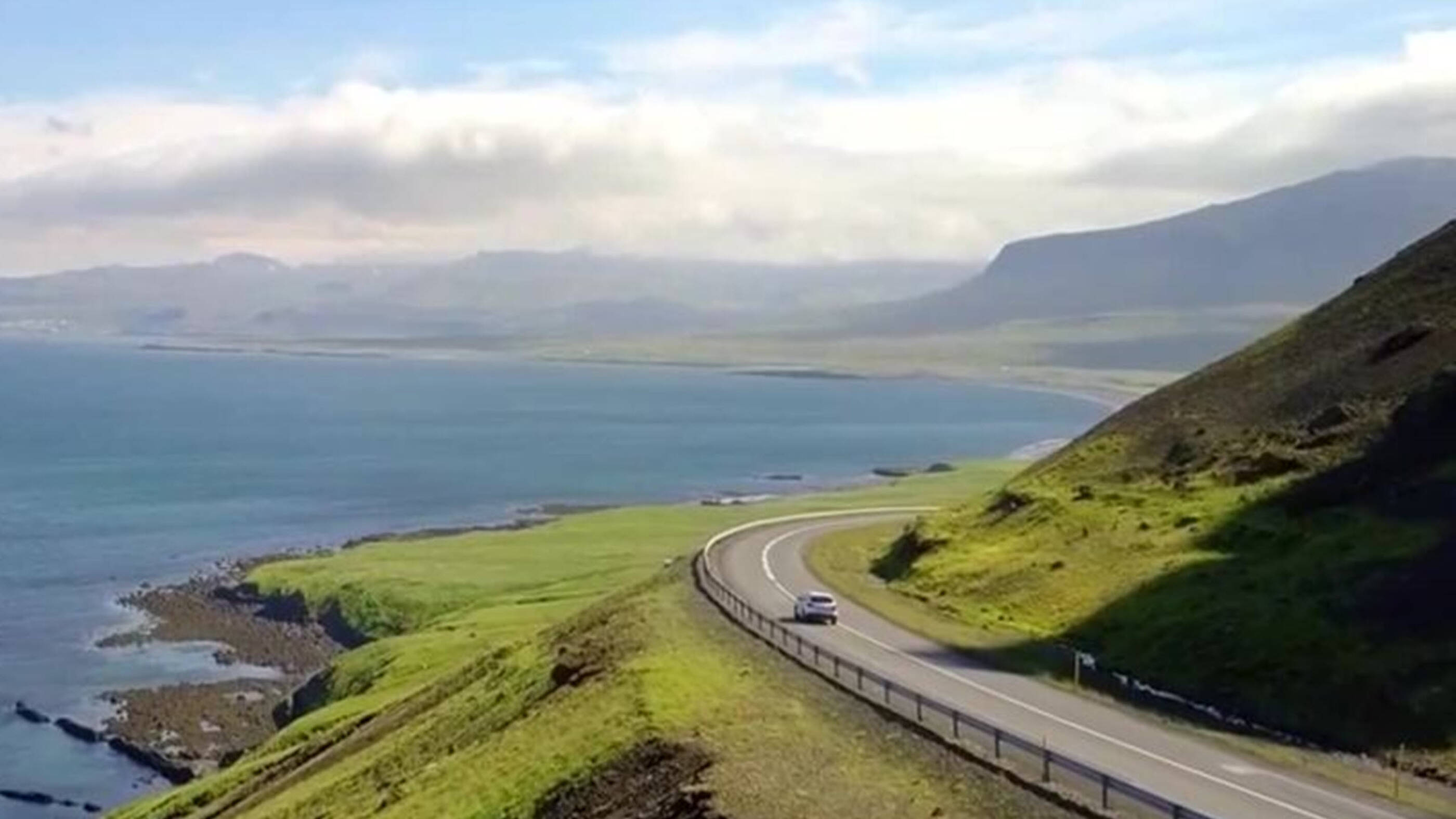 Car driving on road between mountains and ocean